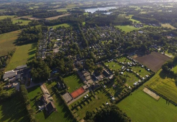 Luftfoto af et lodgeområde med grønne marker, bygninger og træer under en lys himmel i landskabet.