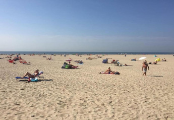 Mensen ontspannen op een brede zandstrand vlakbij de kust in Nederland, met blauwe lucht en zeezicht.