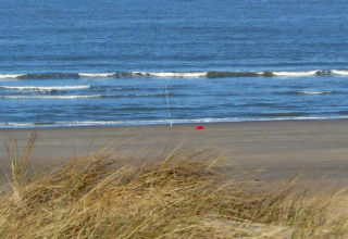 Vista de una playa vacía y el mar con equipo de pesca, desde dunas cerca de un apartamento costero en Holanda.