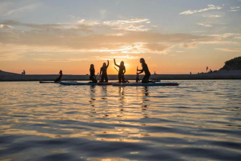Persone fanno paddleboard al tramonto vicino alla costa, accanto a una tiny house nei Paesi Bassi.