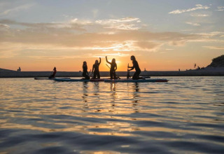 Personas disfrutan del paddle surf al atardecer cerca de la costa junto a una pequeña casa en los Países Bajos.