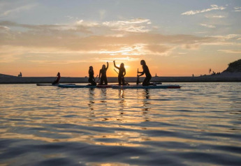 Folk nyder stand-up paddleboarding ved solnedgang nær kysten ved et lille hus i Holland.