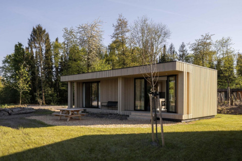 Cabaña moderna de madera rodeada de naturaleza, con mesa de picnic y terraza junto al bosque.