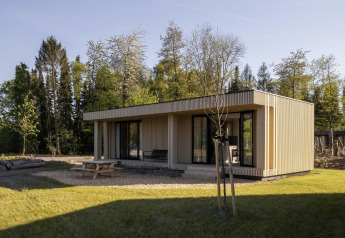 Moderno lodge in legno immerso nella natura, con tavolo da picnic e terrazza vicino alla foresta.