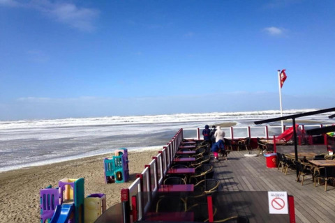 Vista desde la terraza de una cafetería junto a la costa en Países Bajos, con playa, mar y juegos infantiles.