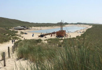 Zicht op een zandstrand met duinen, mensen en speelzone dicht bij de Nederlandse kust.