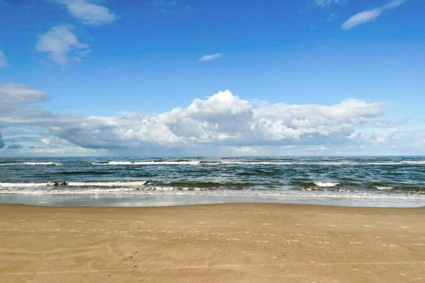 Vista de playa de arena y mar con cielo azul y nubes cerca de un pequeño apartamento en la costa de Países Bajos.