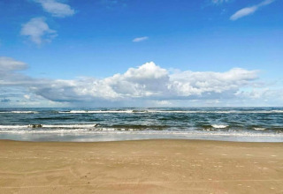 Aussicht auf Sandstrand und Meer mit blauem Himmel und Wolken nahe einer Küstenwohnung in den Niederlanden.