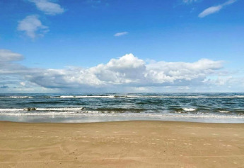 Vista de playa de arena y mar con cielo azul y nubes cerca de un pequeño apartamento en la costa de Países Bajos.