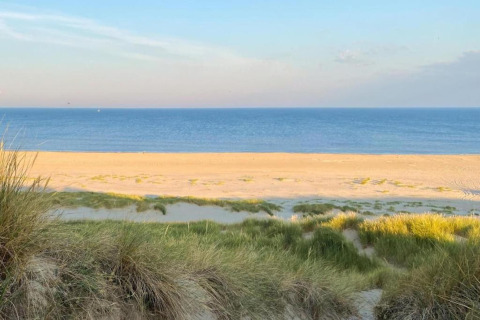 Vista desde las dunas costeras de una tranquila playa de arena y mar azul cerca de la costa de Países Bajos.