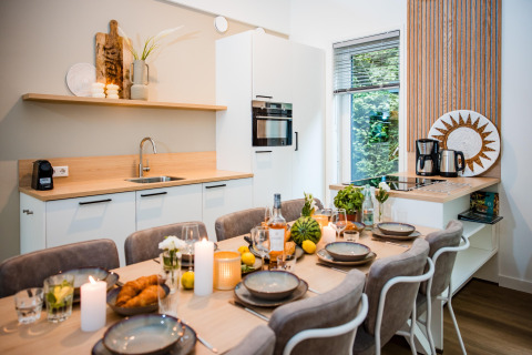 Moderne lodgekøkken med spisebord dækket til seks, stearinlys, mad og naturudsigt gennem vinduet.