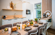 Modernes Lodge-Küche mit gedecktem Esstisch für sechs Personen, Kerzen, Speisen und Blick ins Grüne.