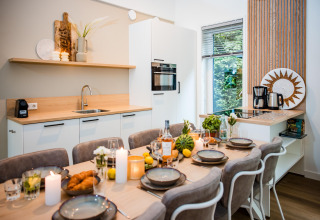 Moderne lodgekøkken med spisebord dækket til seks, stearinlys, mad og naturudsigt gennem vinduet.