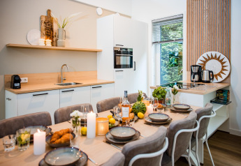 Modern lodge kitchen with a dining table set for six, candles, food, and a window view of greenery.