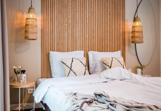 Moderne lodge-soveværelse med dobbeltseng, træpanel, væglamper og hyggelig, afslappende stemning.