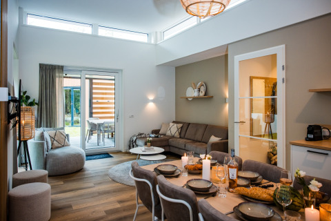 Moderne lodge-stue med spisebord, sofa, store vinduer og adgang til terrasse, hyggelig atmosfære.