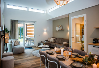 Moderne lodge-stue med spisebord, sofa, store vinduer og adgang til terrasse, hyggelig atmosfære.