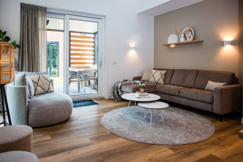 Soggiorno moderno in un lodge con grandi finestre, divano accogliente, tavolini rotondi e decorazioni eleganti.