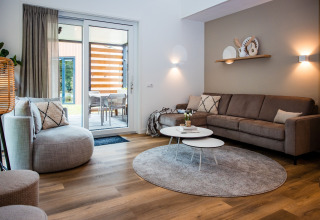 Moderne stue i en lodge med store vinduer, komfortable sofaer, runde borde og et hyggeligt interiør.