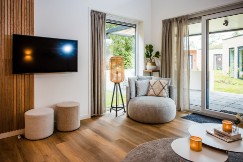 Salon moderne d'un lodge avec fauteuil, TV murale, grandes fenêtres et vue sur le jardin aux Pays-Bas.