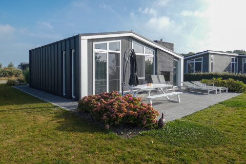 Lodge moderno al Water Resort Oosterschelde 13 con patio arredato, giardino e grandi finestre vetrate.