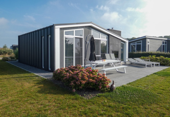 Lodge moderno al Water Resort Oosterschelde 13 con patio arredato, giardino e grandi finestre vetrate.
