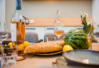 Ein gedeckter Tisch in einer Lodge mit Wassermelone, Baguette, Zitronen, Roséwein und Blumenschmuck.