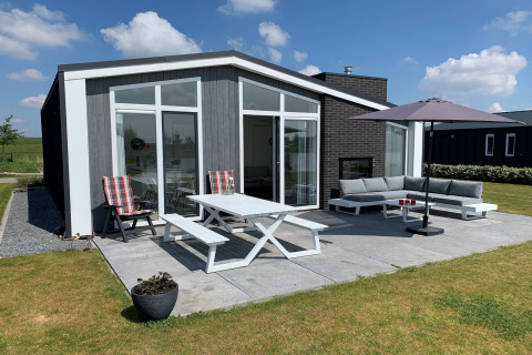 Moderne lodge ved Water Resort Oosterschelde 46 med udendørs terrasse, havesæt, sofa og parasol.