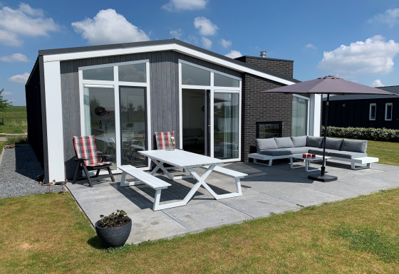 Moderne lodge ved Water Resort Oosterschelde 46 med udendørs terrasse, havesæt, sofa og parasol.
