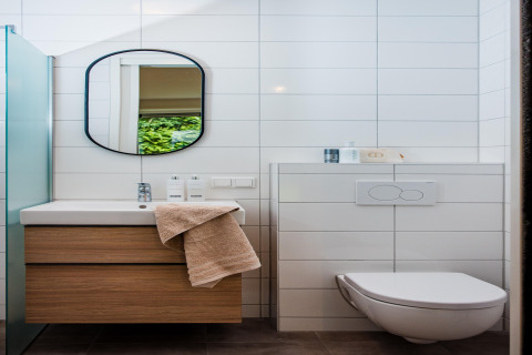 Bagno moderno di una lodge con mobile in legno, specchio, WC sospeso e piastrelle bianche alle pareti.