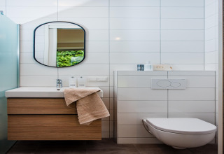 Moderne lodgebadeværelse med træskab, spejl, hængetoilet og hvide vægfliser i minimalistisk stil.