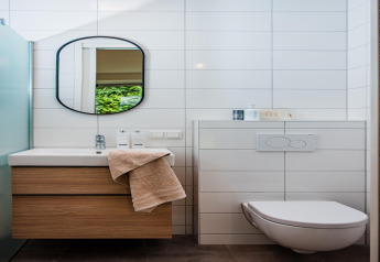 Baño moderno de lodge con mueble de madera, espejo de pared, inodoro flotante y azulejos blancos.