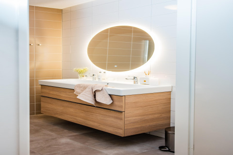 Bagno moderno in un lodge con specchio ovale retroilluminato e mobile lavabo in legno.