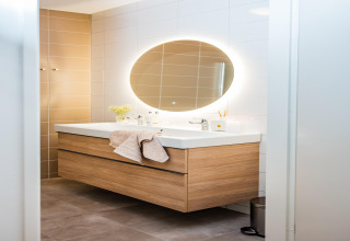 Bagno moderno in un lodge con specchio ovale retroilluminato e mobile lavabo in legno.