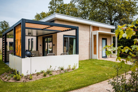 Modernes Lodge-Haus mit Terrasse und Garten, umgeben von Bäumen und Grünfläche in ruhiger Umgebung.