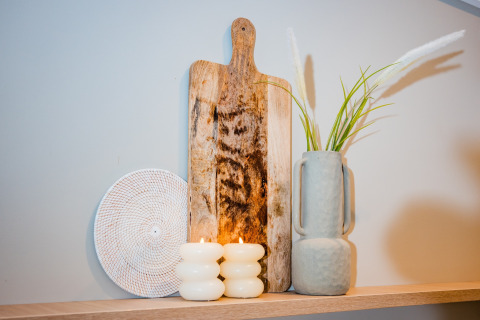 Dekoratives Arrangement mit Holzbrett, Vase mit Gras, weißen Kerzen und geflochtener Platte im Lodge.