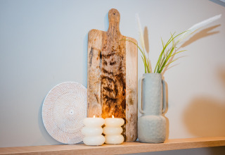Dekoratives Arrangement mit Holzbrett, Vase mit Gras, weißen Kerzen und geflochtener Platte im Lodge.