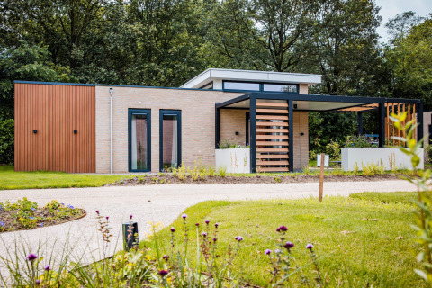 Moderne Lodge mit Holz- und Glasfassade, umgeben von grünem Garten und Blumen, in ruhiger Natur gelegen.