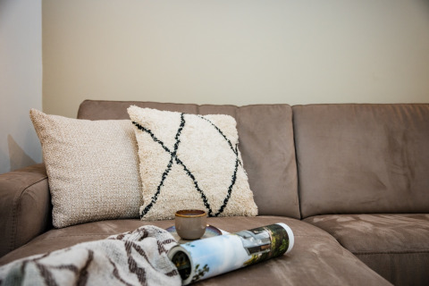 Blød beige sofa med to dekorative puder, et tæppe og en kaffekop på et sammenrullet magasin i Voorthuizen.
