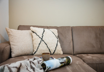Divano beige con due cuscini, plaid, tazza di caffè e rivista arrotolata in un alloggio a Voorthuizen.