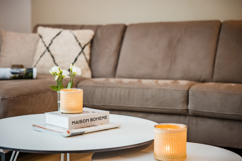 Hyggelig stue med beige sofa, pyntepuder, stearinlys og blomster på et rundt sofabord i Voorthuizen.