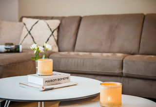 Soggiorno accogliente con divano beige, cuscini, candele accese e fiori su tavolo in casa a Voorthuizen.