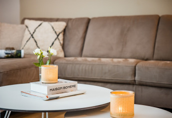 Gemütliches Wohnzimmer mit beiger Couch, Kerzen, Blumen und Bücher auf einem Couchtisch in Voorthuizen.