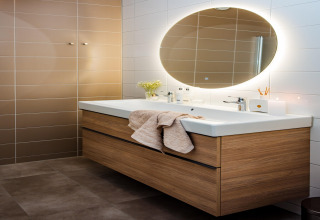 Modernes Badezimmer mit Holzwaschtisch, Doppelwaschbecken, ovalem Spiegel und sanfter Beleuchtung.