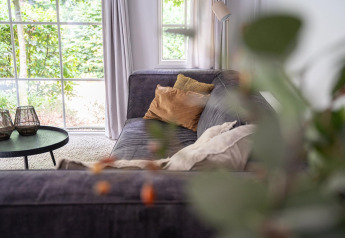 Cozy living room at Heivlinder Comfort 4+2p lodge in the Netherlands, with sofa, cushions and window view.