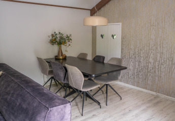 Modern dining area at Heivlinder Comfort 4+2p lodge in the Netherlands, with table, six chairs, and floral decor.