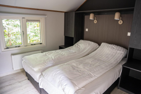 Slaapkamer in Heivlinder Comfort 4+2p lodge in Nederland met twee aparte bedden, raam en moderne stijl.