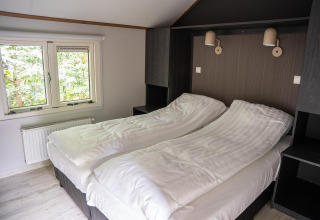 Slaapkamer in Heivlinder Comfort 4+2p lodge in Nederland met twee aparte bedden, raam en moderne stijl.