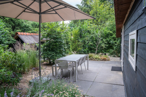 Buitenterras met tafel, stoelen en grote parasol aan de Heivlinder Comfort lodge in Nederland.