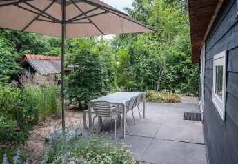 Outdoor patio with table, chairs, and large umbrella at Heivlinder Comfort lodge in the Netherlands.
